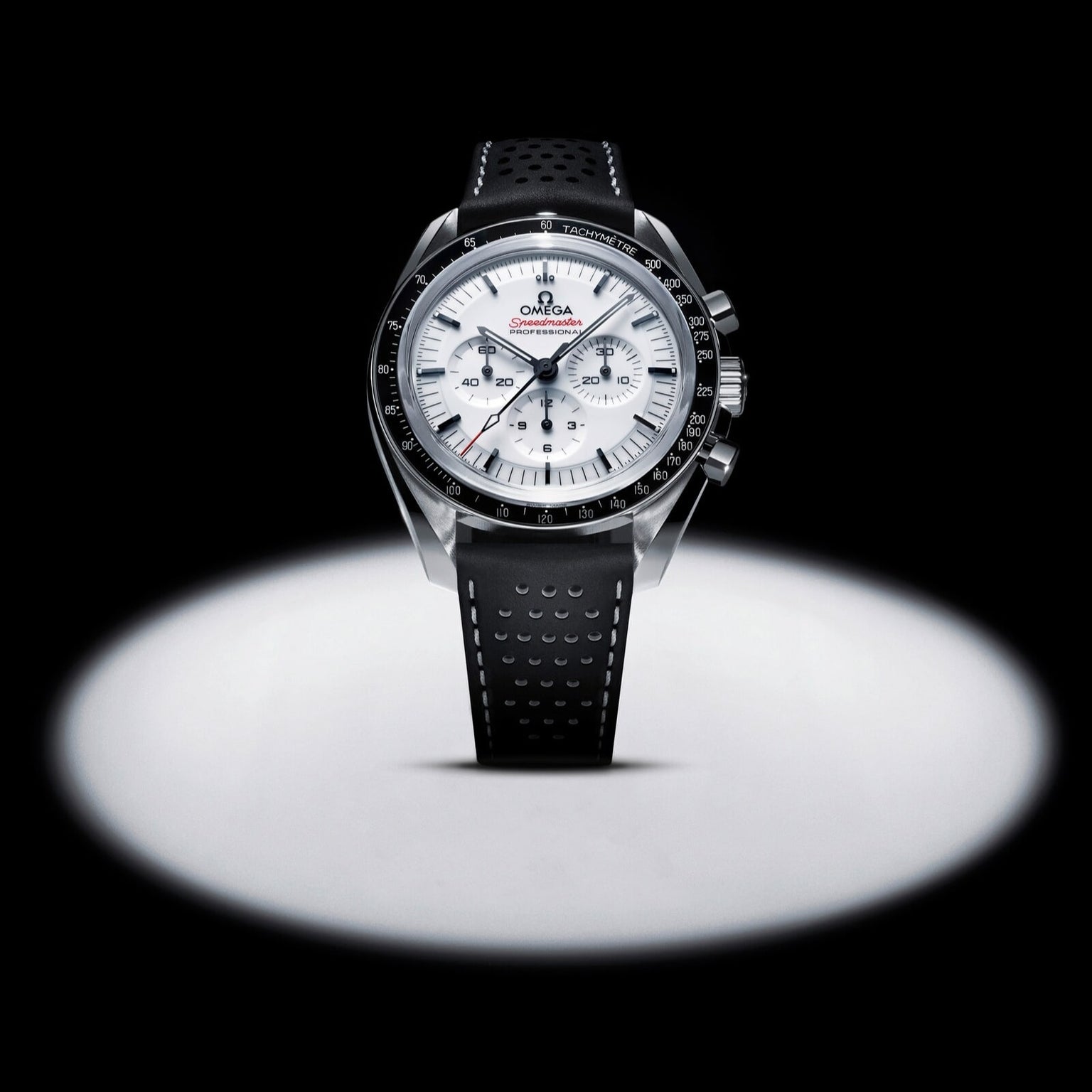 An OMEGA Speedmaster Moonwatch Professional chronograph, featuring a black and white dial and a perforated leather strap, is displayed upright in a spotlight against a black background.