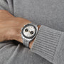 A person wearing an OMEGA Speedmaster Chronoscope Paris 2024 Olympics watch with a white dial and black subdials, dressed in a grey knit sweater.