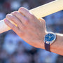 A close-up of a person’s hand gripping a pole, wearing an OMEGA Seamaster Aqua Terra 150M wristwatch with a blue face and stainless steel case.