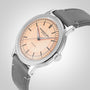 The Raymond Weil Millesime Automatic with a salmon sector dial and grey leather strap highlights Swiss luxury watchmaking against a white backdrop.