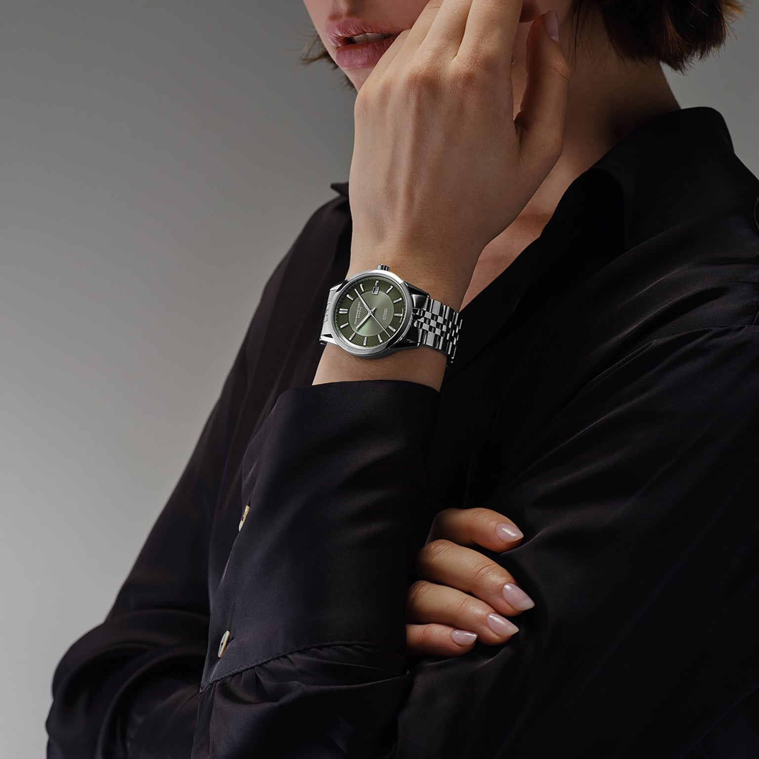 A person in a black shirt displays the Raymond Weil Freelancer Automatic Olive Green Dial watch, hand near chin, against a neutral background.