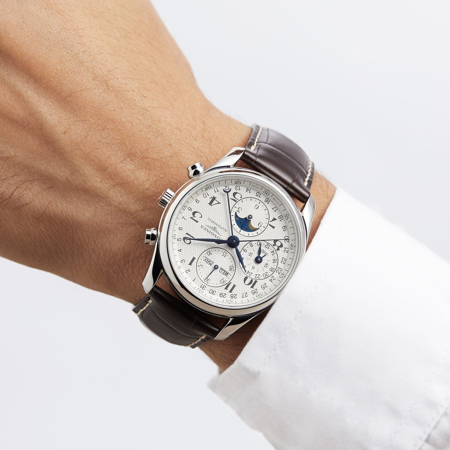 A wrist wearing the Longines Master Collection Chrono Moonphase watch, featuring multiple dials and a stainless steel case, paired with a white dress shirt.