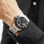 A person in a black long-sleeve shirt wears a Longines HydroConquest watch with a stainless steel case, black dial, and silver bracelet on their left wrist.