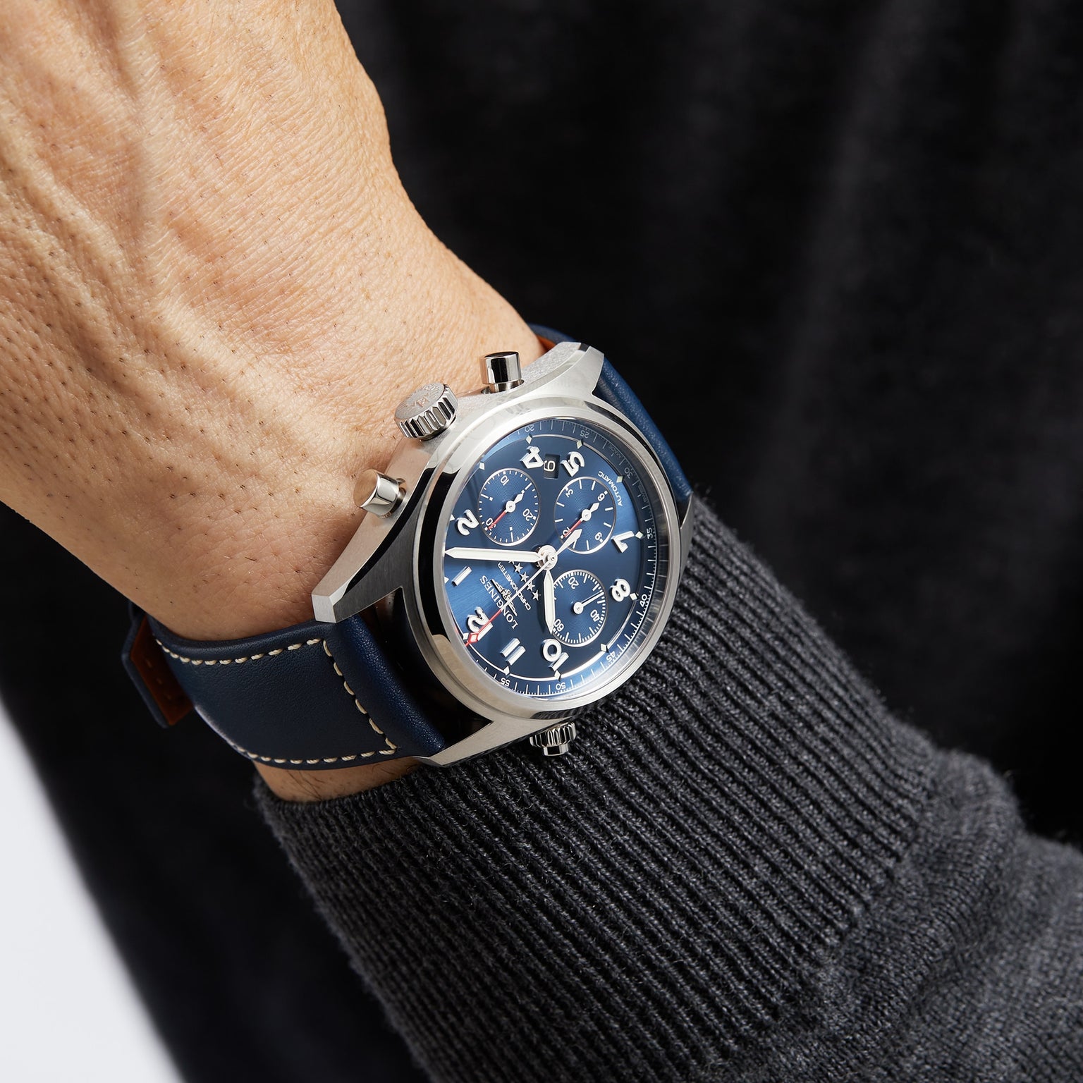 A person wearing a Longines Spirit Chronograph watch with a 42mm stainless steel case and a dark blue leather strap on their left wrist.