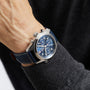 A person wearing a Longines Spirit Chronograph watch with a 42mm stainless steel case and a dark blue leather strap on their left wrist.