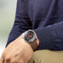Someone in a dark blue sweater and beige pants displays a Longines Legend Diver watch with a brown leather strap and black dial on their left wrist.