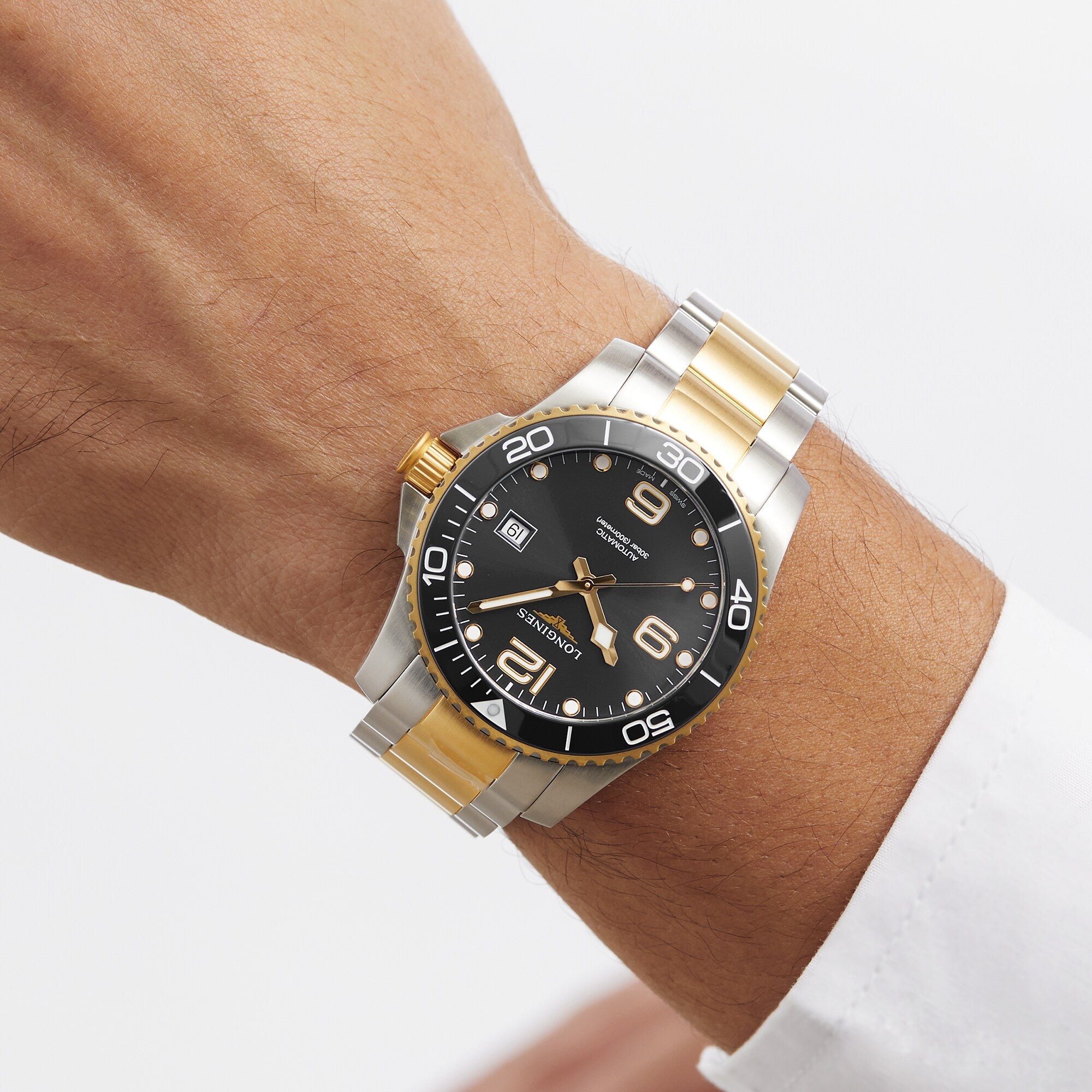 A Longines HydroConquest diving watch in silver and gold, with a black dial and date display, is worn on the left wrist above a white shirt cuff.