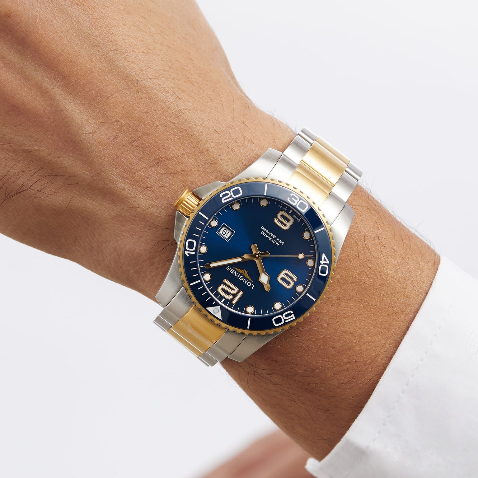A wrist wearing a Longines HydroConquest two-tone silver and gold diving watch with a blue dial, date display, and rotating bezel against a plain background.
