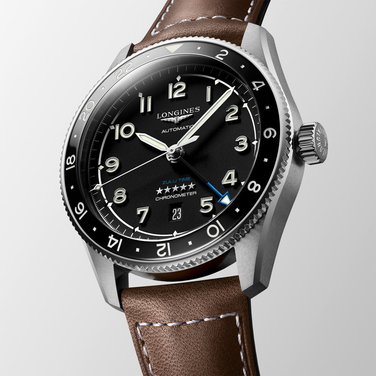 The Longines Spirit Zulu Time automatic watch features a black dial with white numerals, a stainless steel case, brown leather strap, and date display at 6 o’clock.