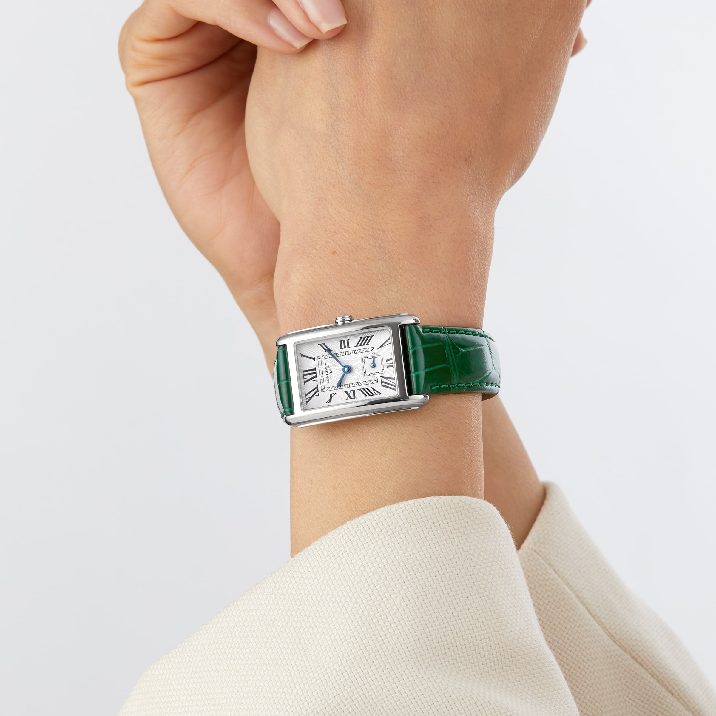 A person wearing a Longines DolceVita watch with a silver rectangular case, green leather strap, Roman numerals, and quartz movement on their left wrist.