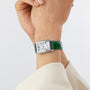 A person wearing a Longines DolceVita watch with a silver rectangular case, green leather strap, Roman numerals, and quartz movement on their left wrist.