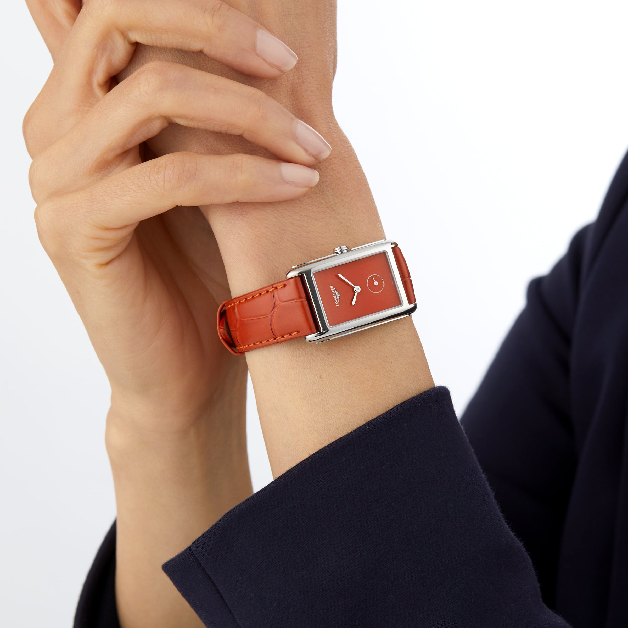 A person in a dark long-sleeve outfit wears the Longines DolceVita Monochrome—a rectangular red quartz watch with a leather strap—radiating timeless elegance.