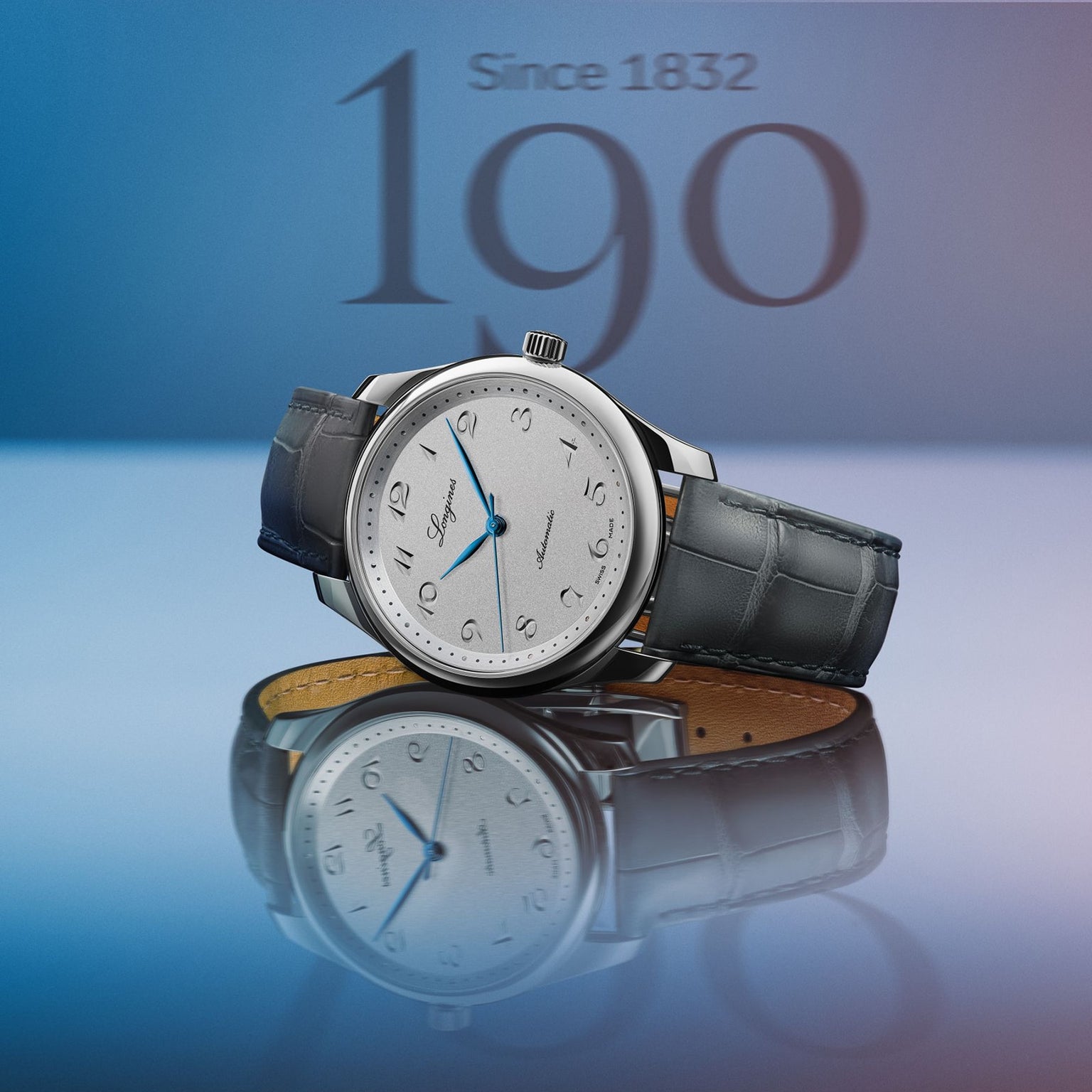A Longines Master Collection luxury wristwatch with a blue leather strap and silver dial is showcased against a blue background, featuring Since 1832 and bold 190 text behind it to highlight its exclusivity.