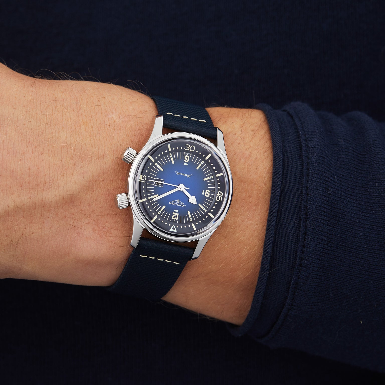 A person in a dark long-sleeve shirt wears a Longines Legend Diver—featuring a blue dial, silver case, black strap, and automatic movement—on their left wrist.