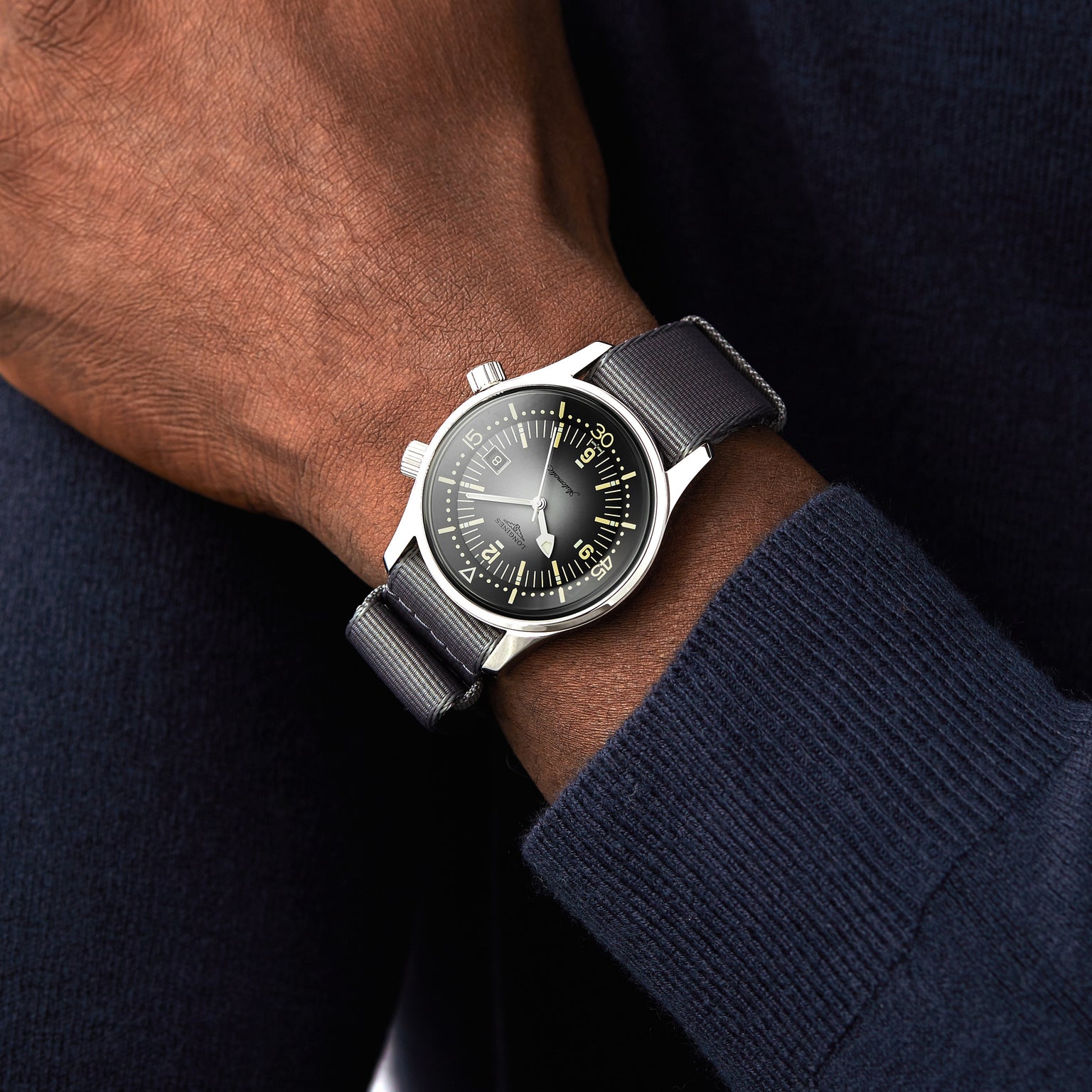 A person wearing a Longines Legend Diver watch with a black face and black strap on their left wrist, paired with a dark blue sweater.