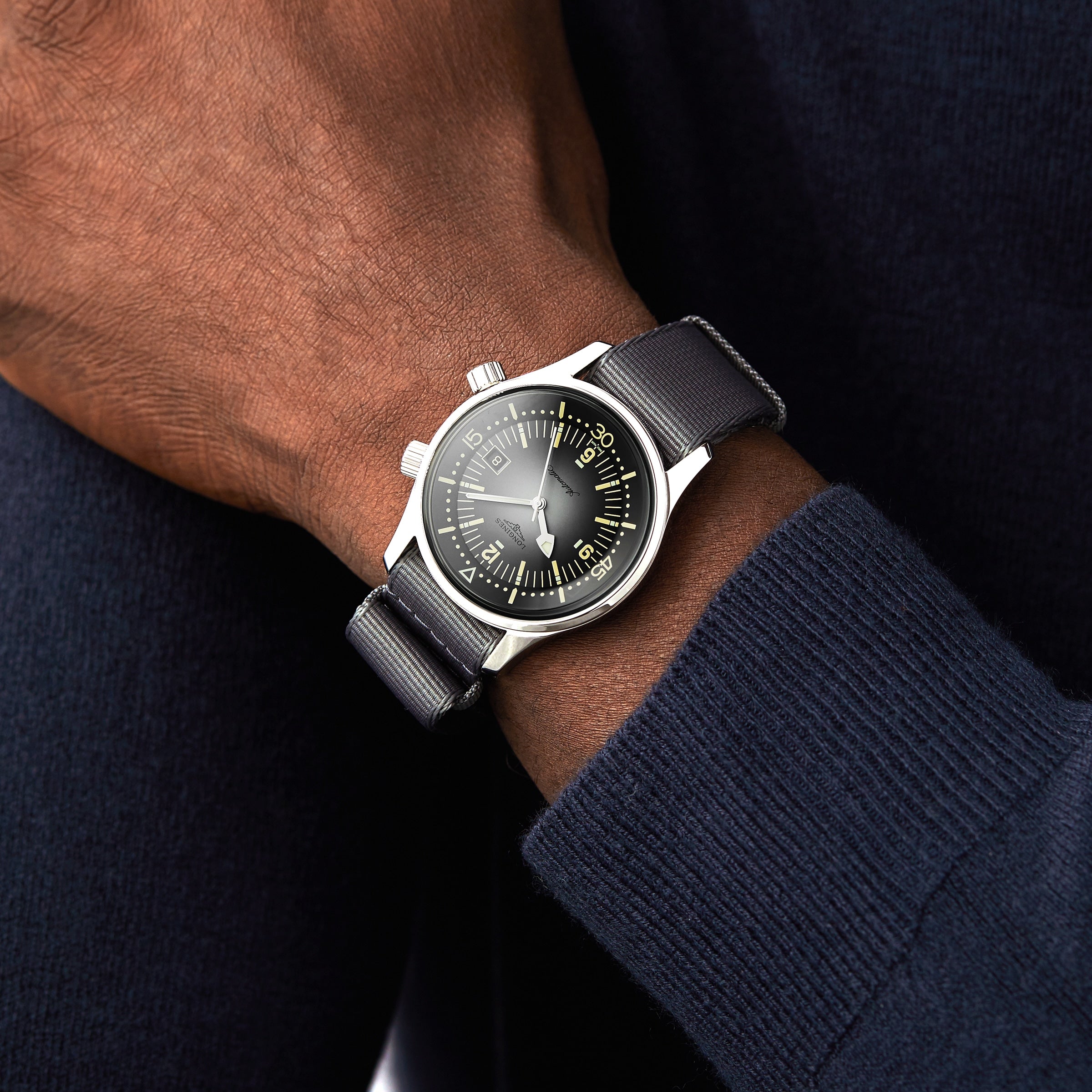 A person wearing a Longines Legend Diver watch with a black face and black strap on their left wrist, paired with a dark blue sweater.