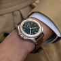 A close-up of a person wearing the Longines Pilot Majetek, featuring a brown leather strap, black dial, gold numerals, and small seconds subdial—reflecting aviation heritage against a tan sleeve.