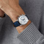 A person wearing a Longines Master Collection Chrono Moonphase silver chronograph with a blue leather strap and a light gray knit sweater.