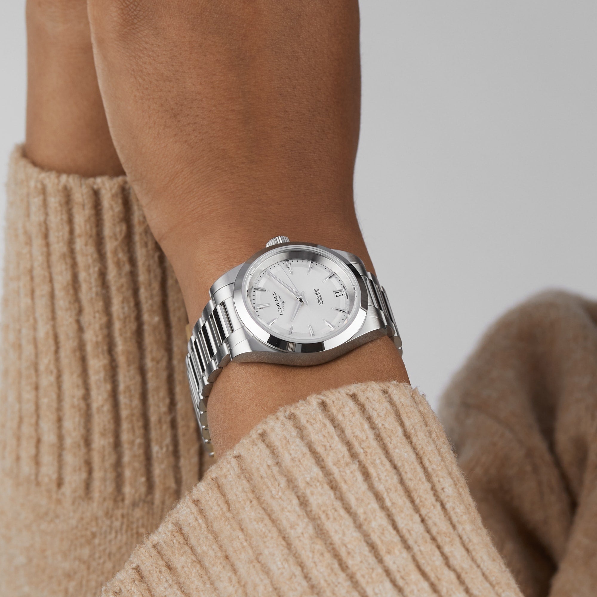 A person in a beige ribbed sweater showcases the Longines Conquest on their left wrist.
