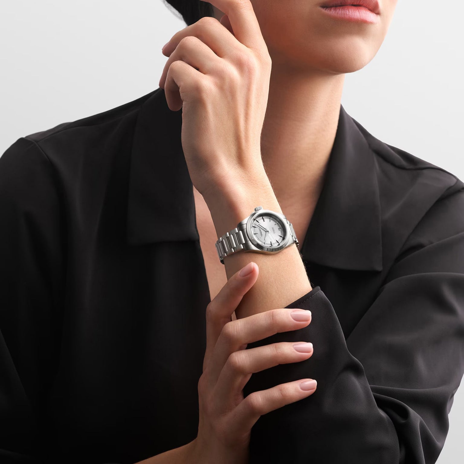 A person in a black collared shirt showcases the Longines Conquest watch, which features a stainless steel case, metal band, and a white dial.
