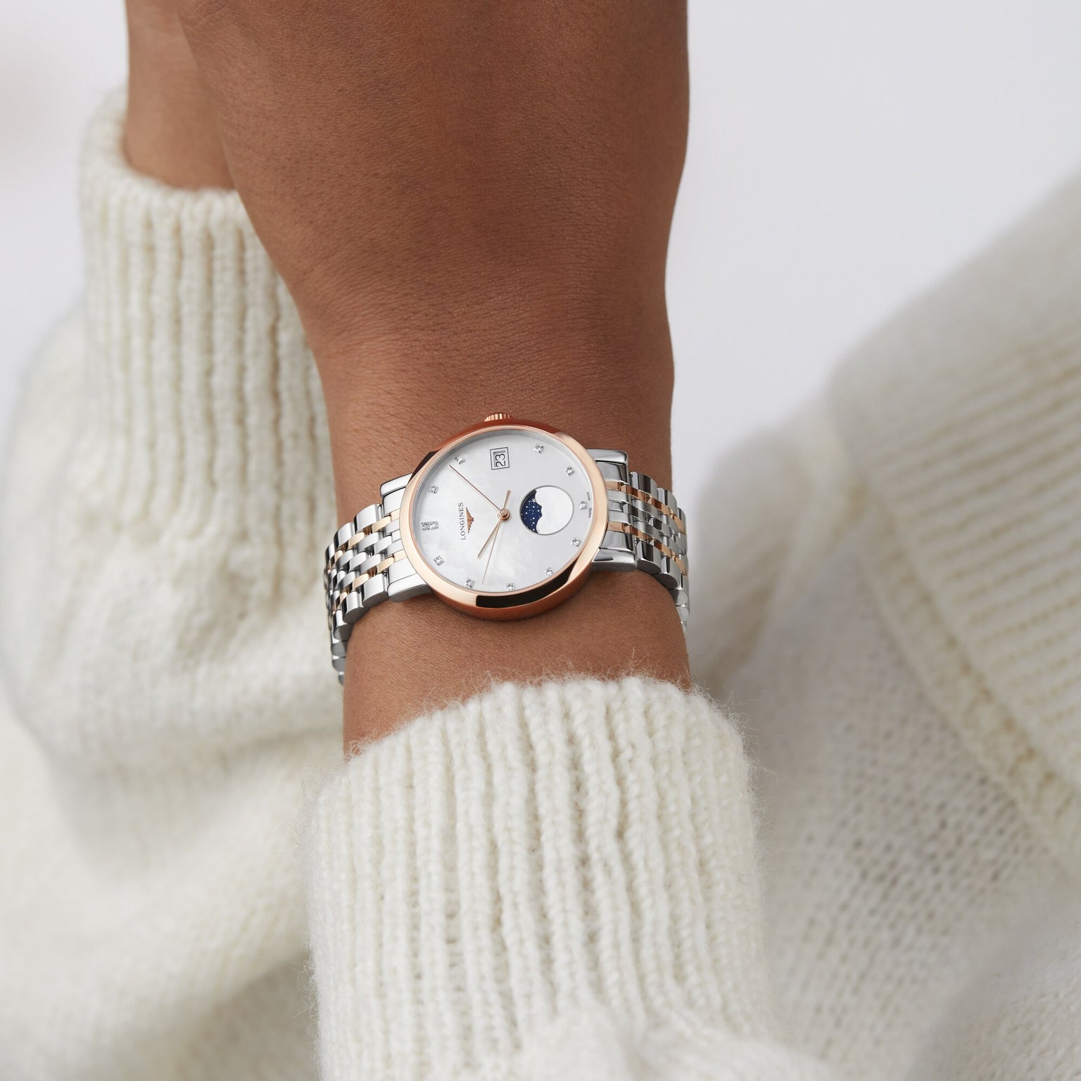 A person wearing the Longines Elegant Collection Moonphase wristwatch, featuring a mother-of-pearl dial, paired with a white knit sweater.