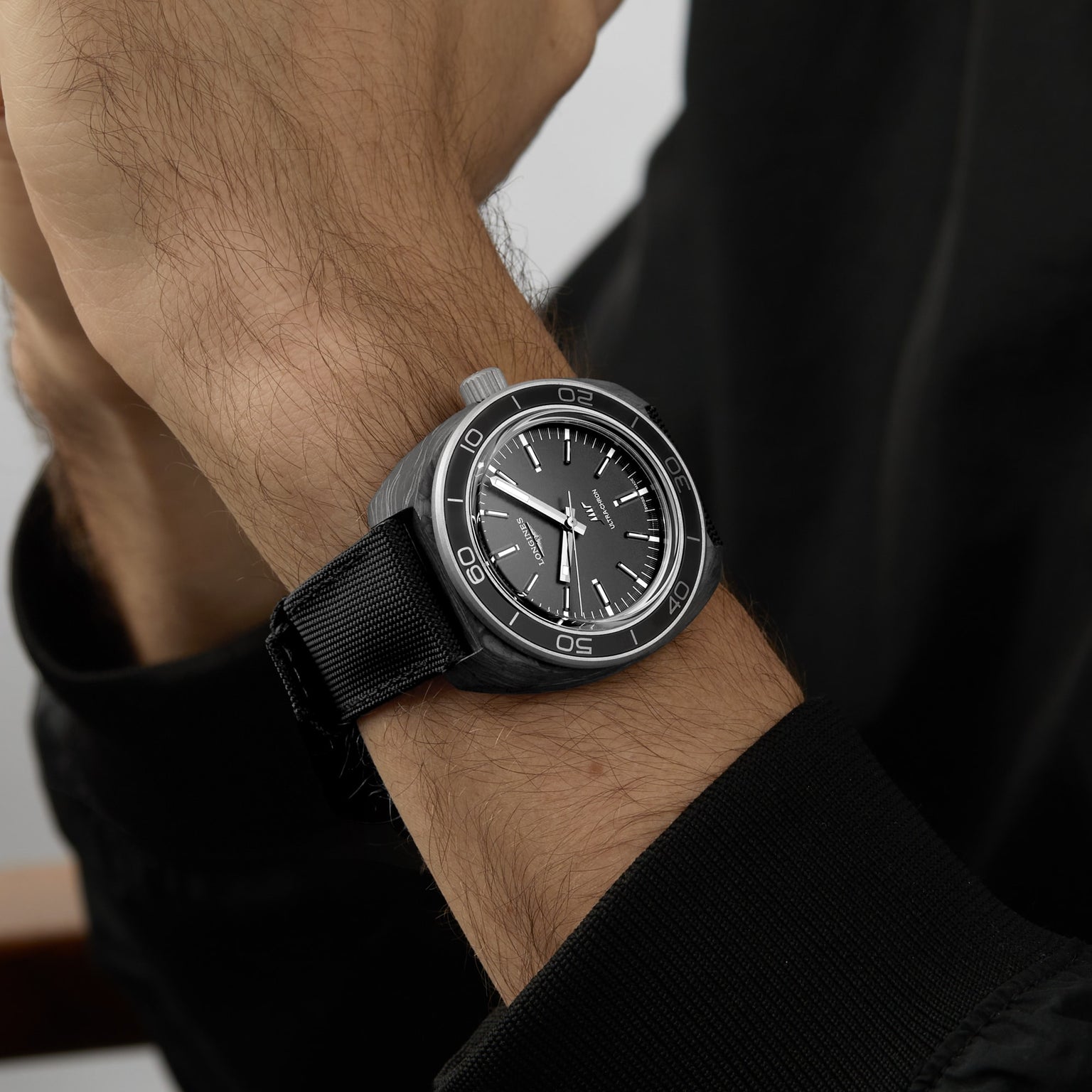 A close-up of a wrist wearing the Longines Ultra-Chron Carbon, featuring a nylon strap and black dial with white hour markers and bezel numbers, known for its high-frequency movement and professional diving features.