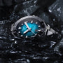 A Tissot Seastar 2000 Professional Powermatic 80 watch with a blue patterned face is partially submerged in dark water, its silver case surrounded by glistening wet rocks.