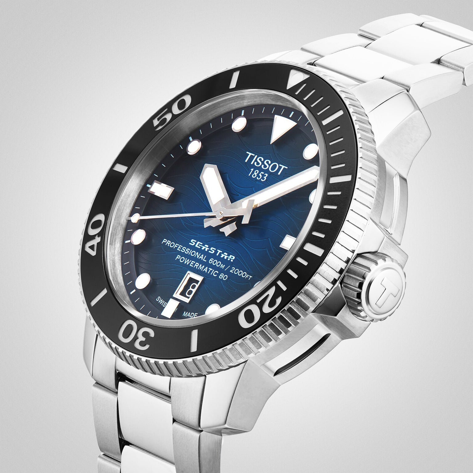 The Tissot Seastar 2000 Professional Powermatic 80 features a blue dial, black rotating bezel, date window, silver stainless steel bracelet, and is powered by the Powermatic 80 movement. Photographed on a light background.