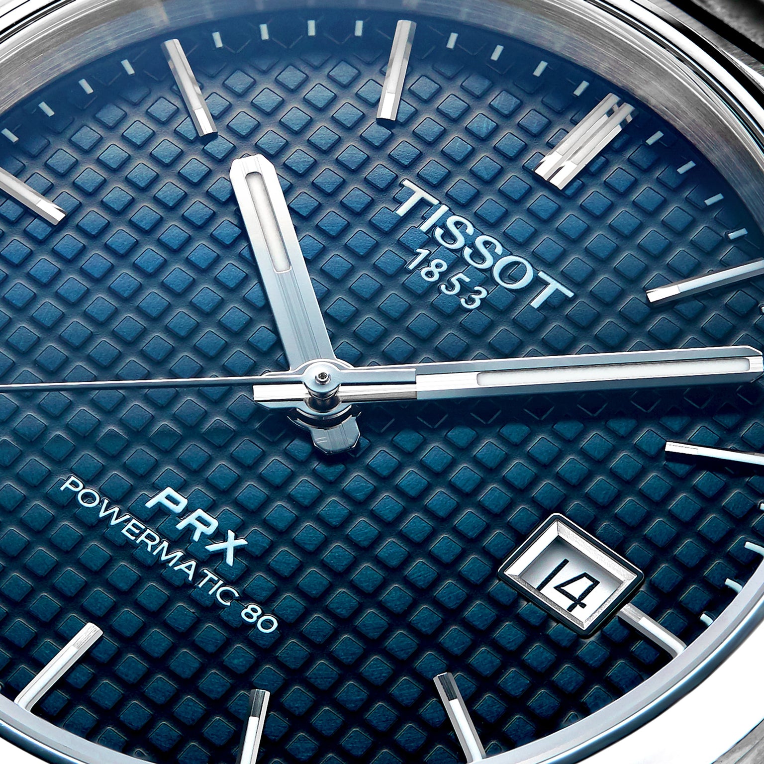Close-up of the Tissot PRX Powermatic 80 watch, featuring a blue textured dial, silver hands and markers, stainless steel case, and a date window displaying 14.