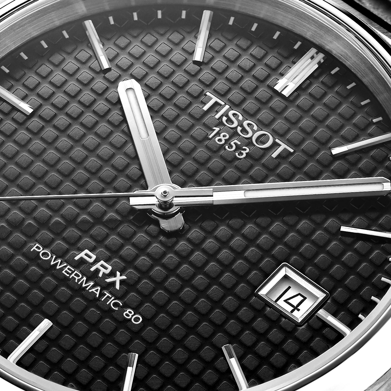 Close-up of the Tissot PRX Powermatic 80 watch face, showcasing its textured black dial with branded markings, silver hands, date window at 3 o’clock, all set in a stylish stainless steel case.