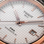 Close-up of a Tissot PRX Powermatic 80 watch face featuring a textured white dial, rose gold hands and markers, stainless steel case, and date window displaying the number 4.