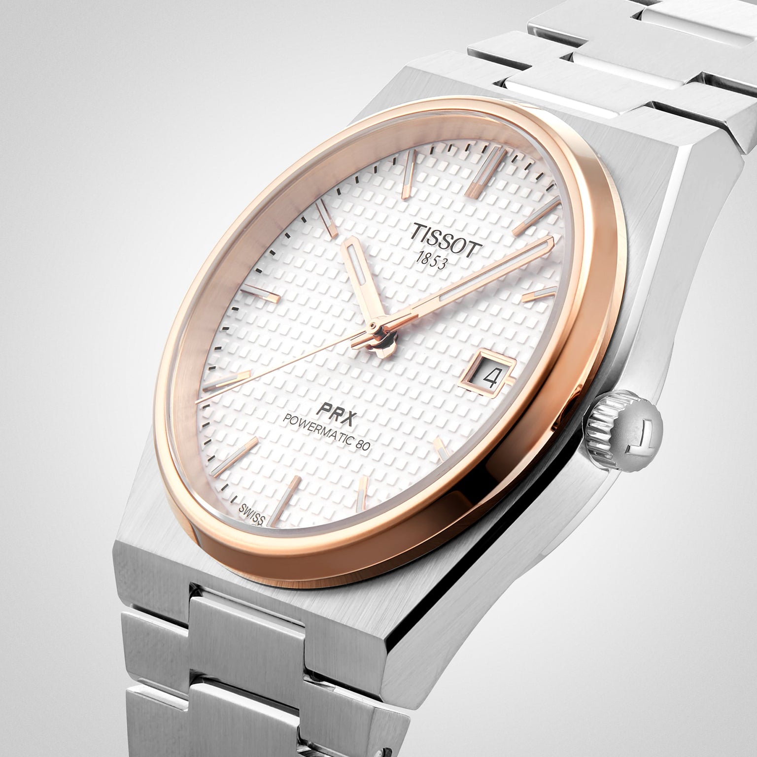 A close-up of the Tissot PRX Powermatic 80 wristwatch featuring a stainless steel case, rose gold accents, a white textured dial, and a date display at 3 o’clock.