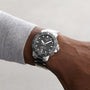 A person wearing a Tissot Seastar 1000 Powermatic 80 wristwatch with a black face and metal band on their left wrist, shown against a plain background.