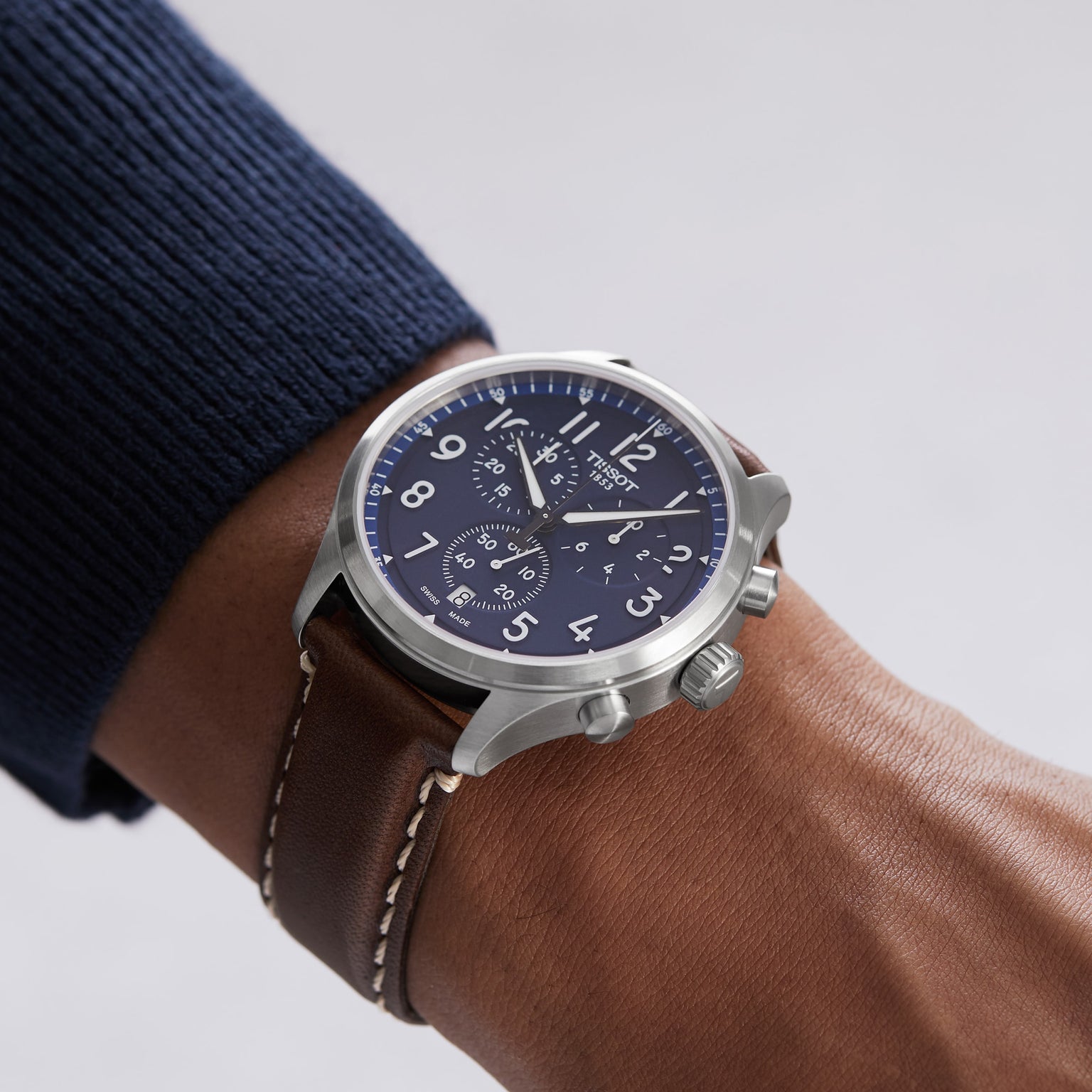 A person wearing the Tissot Chrono XL Vintage, an elegant timepiece with vintage-inspired design, a silver case, blue dial, and brown leather strap on their left wrist.