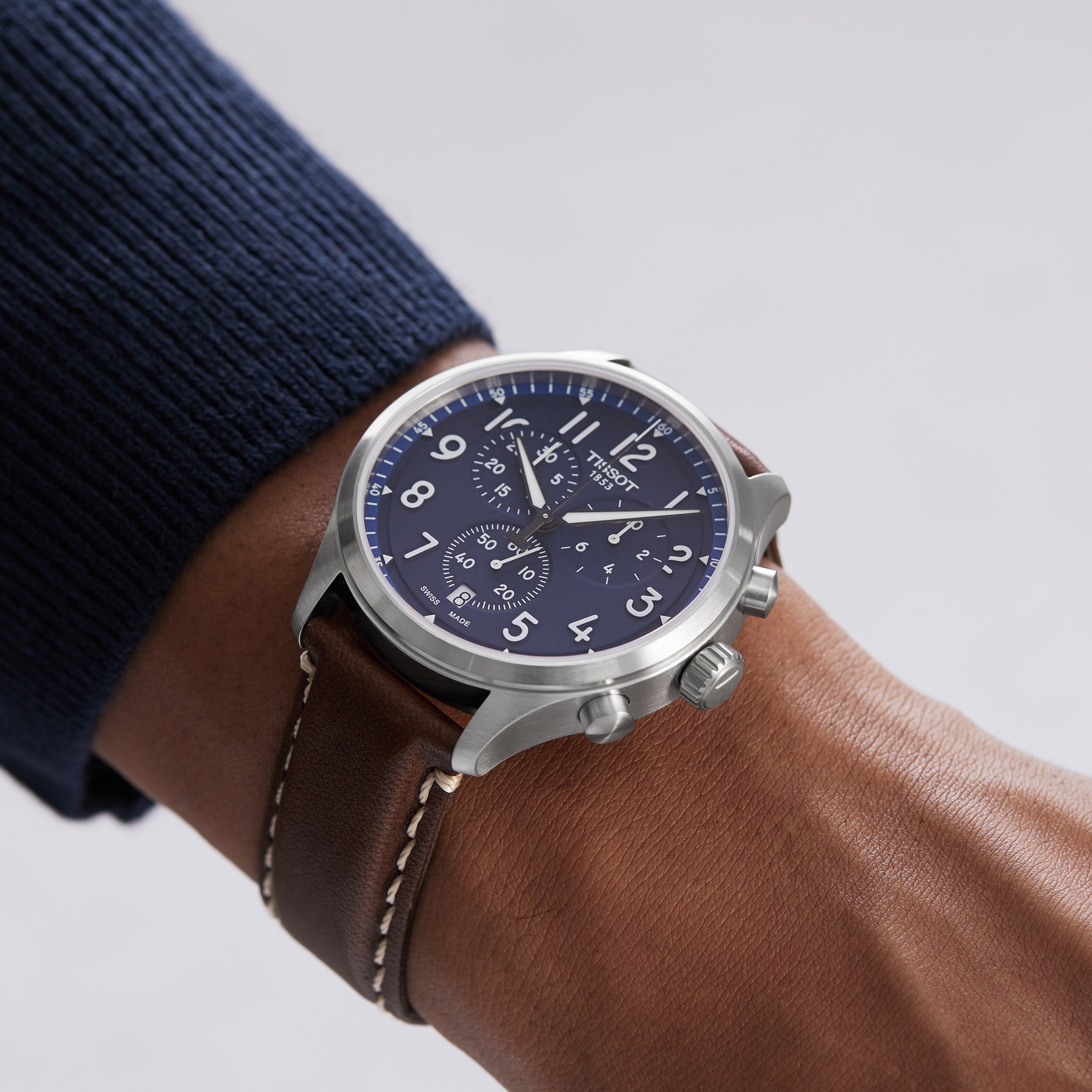 A person wearing the Tissot Chrono XL Vintage, an elegant timepiece with vintage-inspired design, a silver case, blue dial, and brown leather strap on their left wrist.