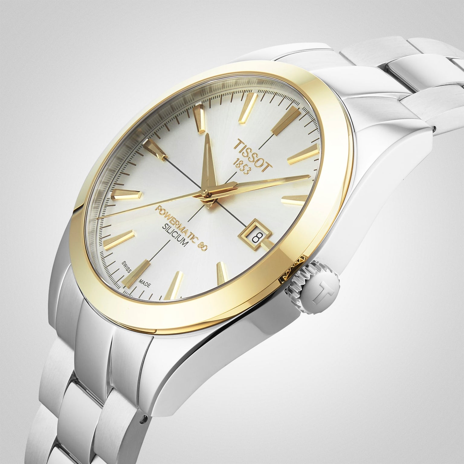 The Tissot Gentleman Powermatic 80 Silicium features a white dial with gold hour markers, an 18K gold bezel, date display at 3 o’clock, and a stainless steel band.