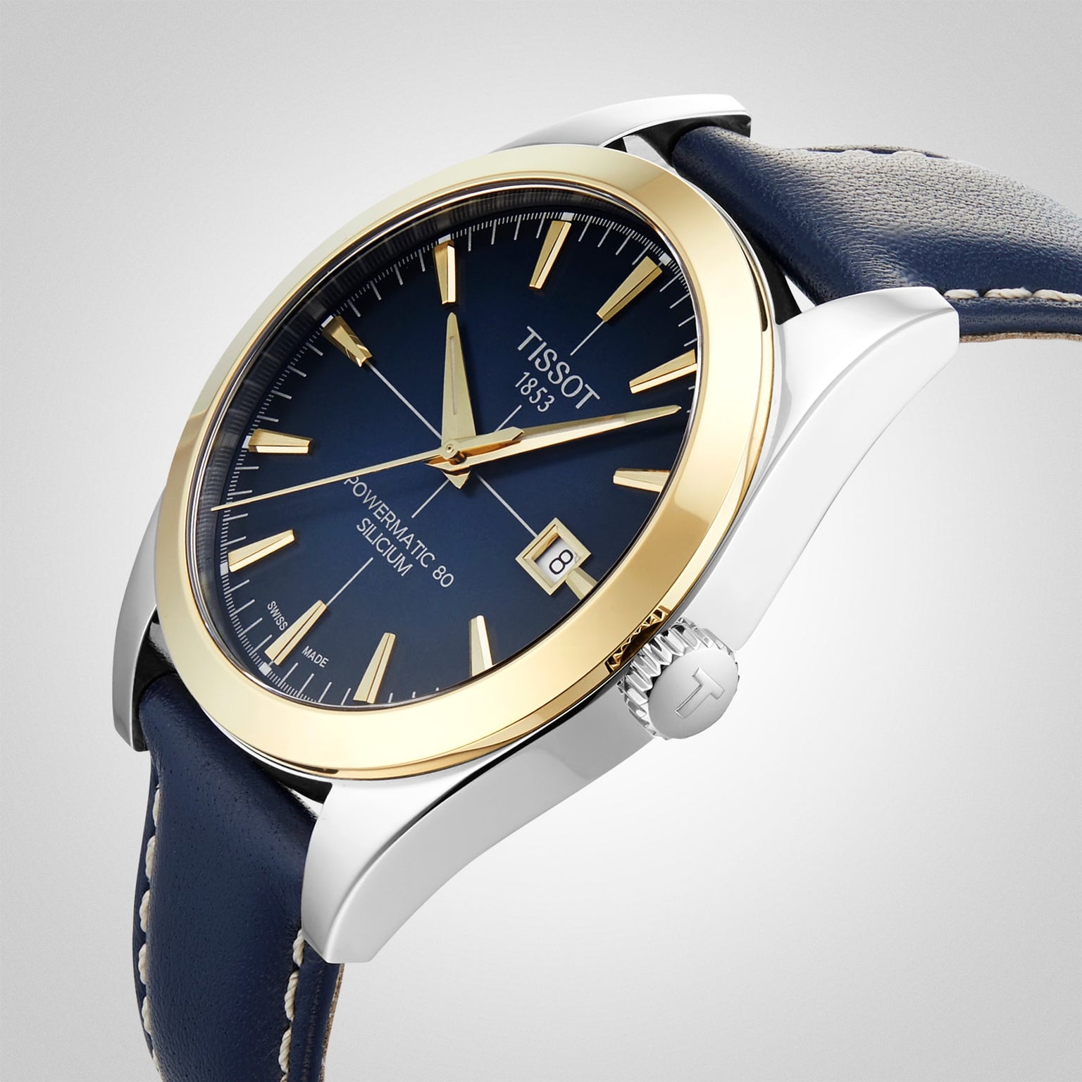 A close-up of the Tissot Gentleman Powermatic 80 Silicium wristwatch, featuring a blue face, solid 18k gold bezel, and a blue leather strap.