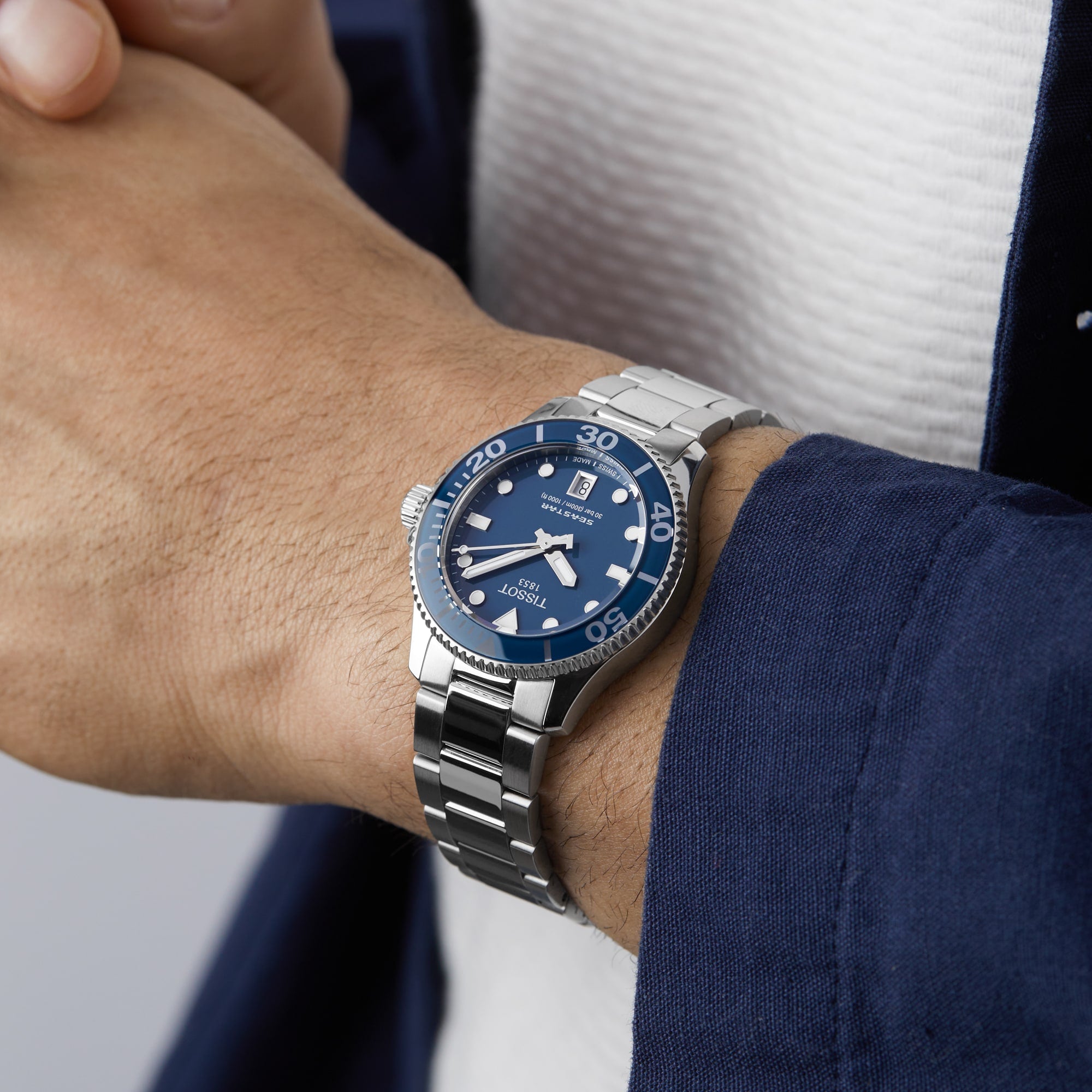 A person wearing a Tissot Seastar 1000 watch with a silver and blue design, metal band, showing the time as about 10:09.