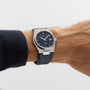Someone wears a Tissot PRX Powermatic 80 with a black dial, stainless steel case, and leather strap on their left wrist—a striking luxury watch.