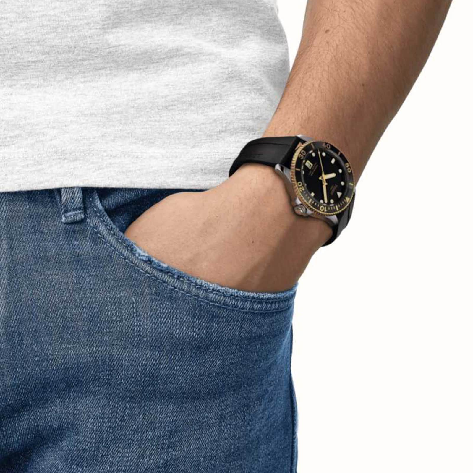A person in jeans and a white shirt has their hand in their pocket, wearing a Tissot Seastar 1000 wristwatch.