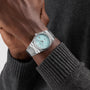 A person wearing the Tissot PRX Powermatic 80 with a stainless steel case, light blue dial, and silver band, dressed in a dark gray sweater.