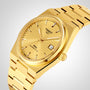 The Tissot PRX Powermatic 80 wristwatch features a patterned gold dial, date display, gold metal bracelet, and advanced Nivachron hairspring for enhanced precision, displayed at an angle against a neutral background.