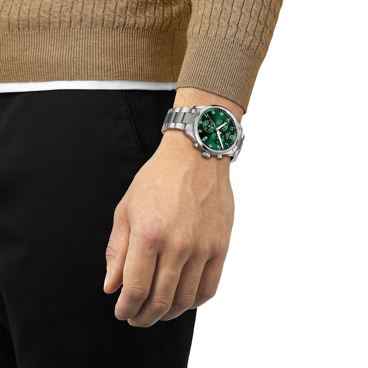 A person in a brown sweater and black pants showcases a Tissot Chrono XL Classic with a green dial and large case on their left wrist.
