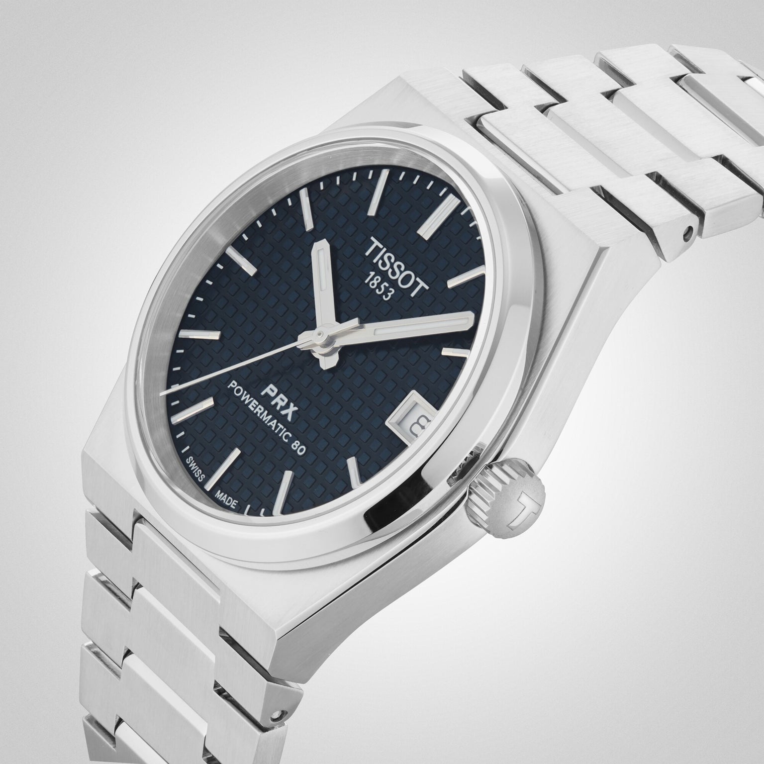 The Tissot PRX Powermatic 80 showcases a stainless steel case, textured blue dial, silver markers, date window at 3 o’clock, and a stylish metal bracelet.