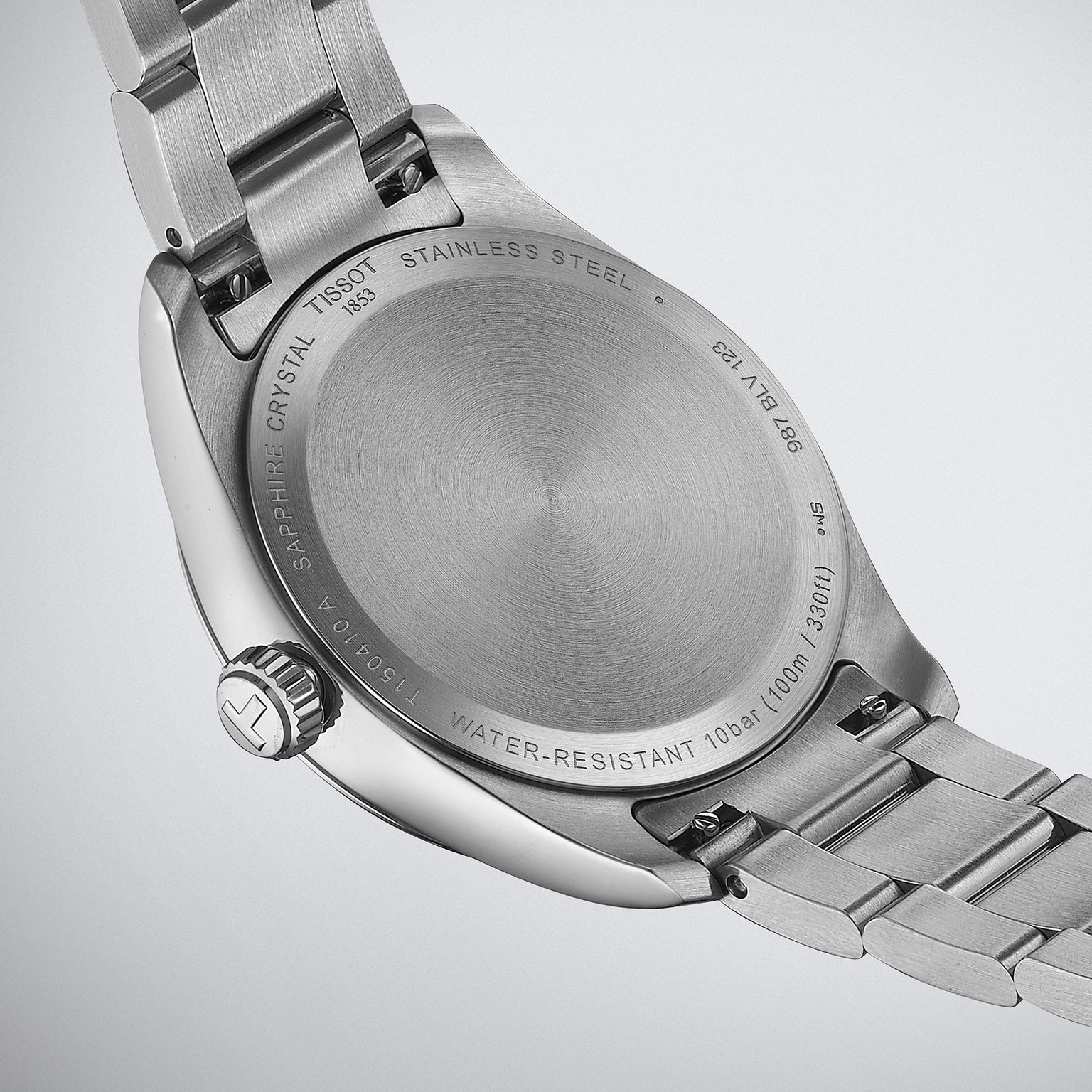 Close-up of the back of a Tissot PR 100 stainless steel wristwatch, featuring engravings detailing water resistance, scratch-resistant sapphire crystal, Swiss Quartz movement, and model information.