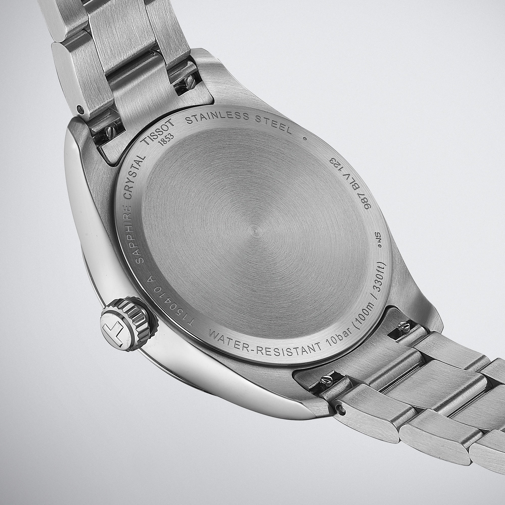 Close-up of the back of a Tissot PR 100 stainless steel wristwatch, featuring engravings detailing water resistance, scratch-resistant sapphire crystal, Swiss Quartz movement, and model information.