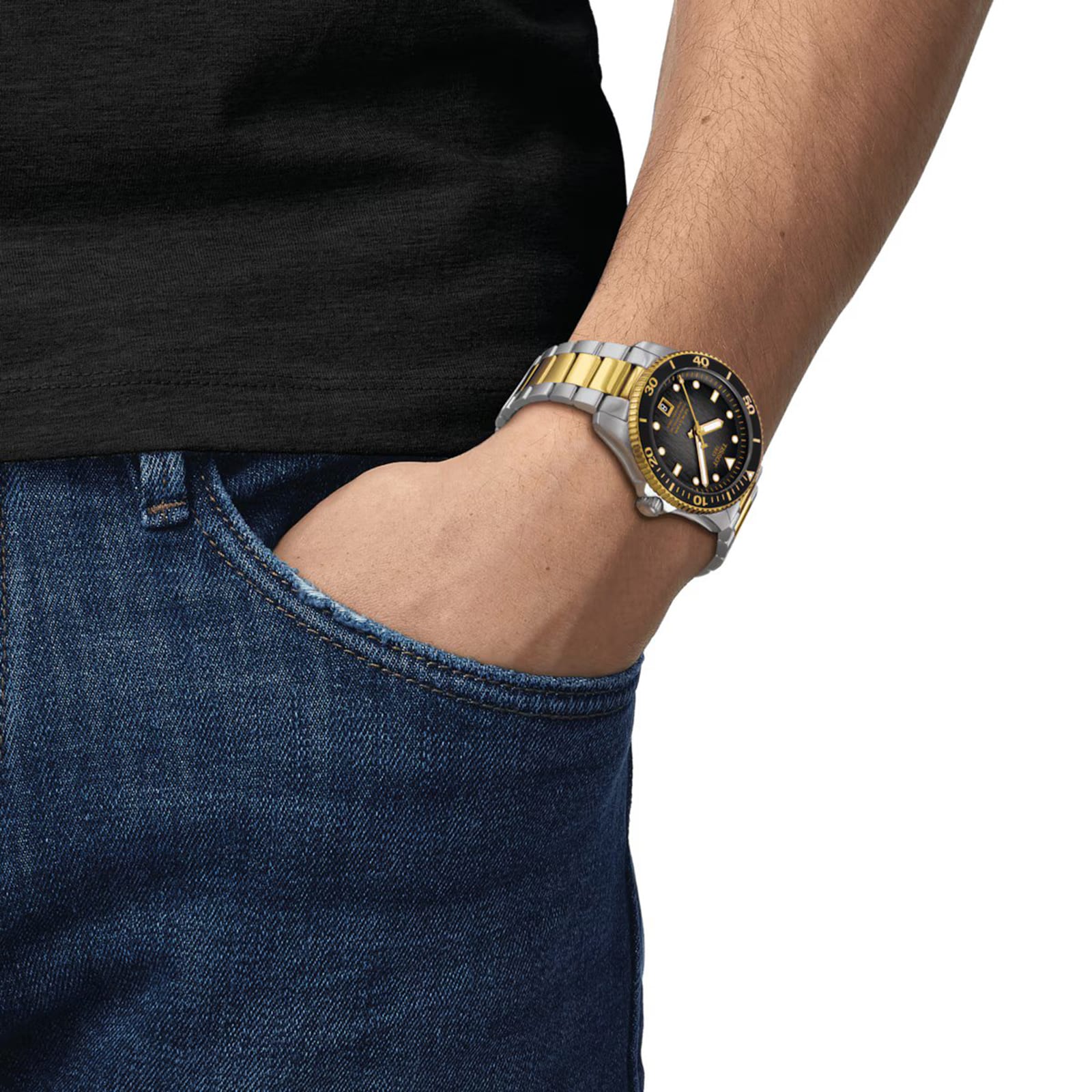 A person in blue jeans, a black shirt, and a Tissot Seastar 1000 Powermatic 80 watch with a black and gold bezel accented by Super-LumiNova, their hand in their pocket.