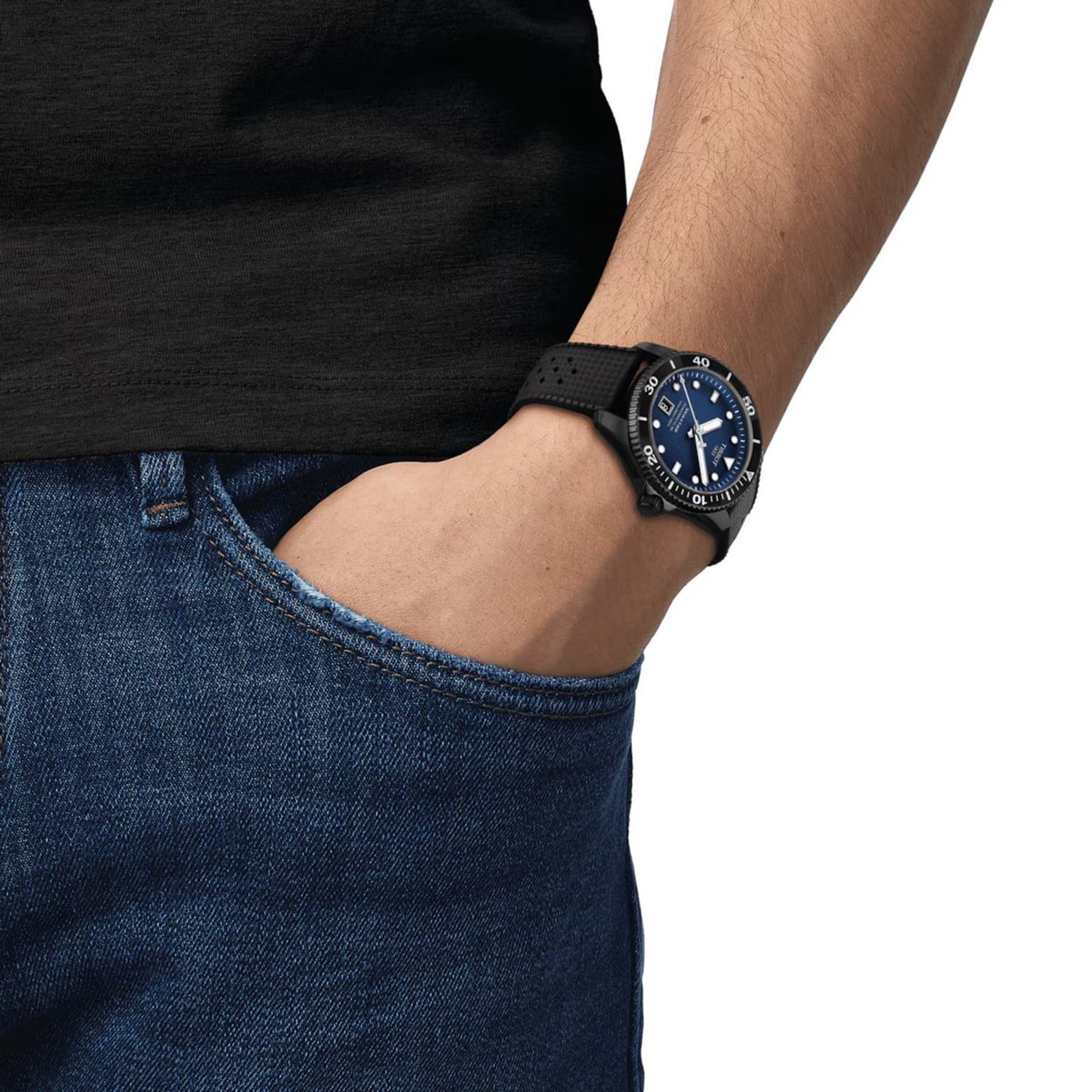 A person wearing a black short-sleeve shirt and blue jeans has their left hand in their pocket, showcasing a Tissot Seastar 1000 Powermatic 80 with a striking blue dial.