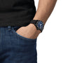 A person wearing a black short-sleeve shirt and blue jeans has their left hand in their pocket, showcasing a Tissot Seastar 1000 Powermatic 80 with a striking blue dial.