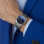 A person in a blue suit and light blue shirt wears the Tissot PRX Powermatic 80, featuring a silver case, blue textured dial, sapphire crystal, and metal bracelet on their left wrist.